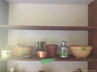 Shelf with various kitchenware and decorative items including ceramic bowl, copper container, tin jug, lantern, terracotta pot, decorative container with horse design and wooden box.