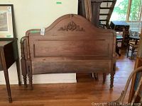 Full view of wooden double bed headboard showing carved molding, arched top, turned posts, and warm medium brown finish.