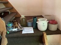 Various pottery crocks including two with lids; bowls and trays are visible; a reflective silver tray with blue and brown bowls on it; the red lid crock is prominent