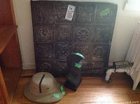 Photo showing all four items together: metal statue, pith helmet, decorative metal roof sheet and rusted sword leaning with handle visible