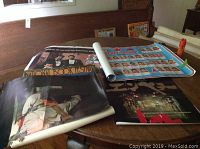 Four vintage posters laid out on a round wooden table with visible curling and folds.
