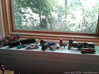 Wide view of toy cars and collectible miniature vehicles on a windowsill, including trucks, cars, and a Dr Who phone booth model