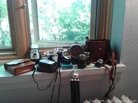 Overall view of vintage cameras, cases, binoculars, light meters, flashes on windowsill