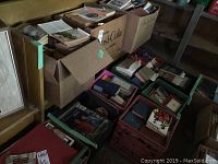 Overall photo of various containers including one large wooden box, two cardboard boxes, and several milk crates filled with books and patterns, showing volume and condition of items.