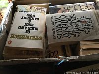 Four small cardboard boxes filled with assorted paperback and hardcover books viewed from above showing condition and variety