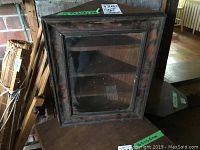 Dark wood glass-enclosed corner cabinet showing front glass door and interior triangular shelves.