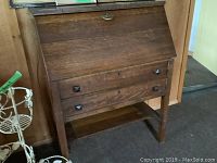 Front view of vintage wooden secretary desk with drop-down writing surface and two drawers.