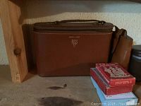 Photo of brown leather wrench case, two small red and blue boxes of playing cards, and brown leather wallet on wooden surface.