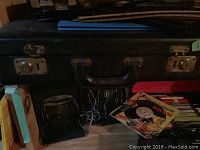 Closed black briefcase with metal latches on top shelf, blue binder and record covers below