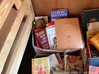 Boxes stacked with French and English books showing titles and covers fresh from a wooden shelving area.