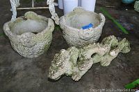 Two Celtic knot concrete planters and one concrete dragon statue shown on concrete floor.
