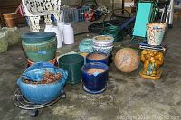 Overall view of assorted planters of various sizes and materials including ceramic, terra cotta, stoneware, plastic, and a plant trolley.