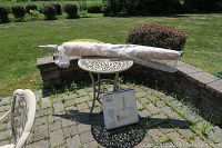 Photo showing the beige folded 8 ft patio umbrella wrapped in protective plastic lying across the cast metal patio table on an outdoor stone patio.