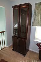 Full view of entire cabinet in room corner, showing dark wood, glass doors, and bottom storage doors.