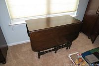 Closed walnut drop leaf table against a wall beneath window. Shows overall size and shape with leaves down.