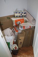 Photo showing corner closet filled with stacked flattened cardboard boxes, biodegradable packing peanuts in clear and orange bag, USPS boxes, paper pads, bubble wrap, tape with dispenser.