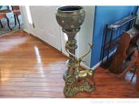 Overview of brass deer sculpture positioned beside enameled brass planter on pedestal.