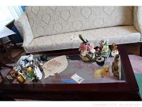 Overview of assorted home decor items on glass coffee table including porcelain box, carved stone dog, ceramic fairy house, and bonsai tree