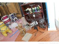 Multiple home decor items on floor including yellow ceramic dog, resin fairy, bust, figure vase, metal tree sculpture with bird, and shelf with ceramic horses