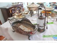 Photo showing the silverplate footed dish with cherub design and handles beside the depression glass pickle jar with metal lid and tongs.