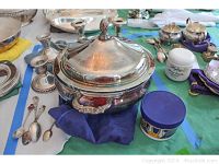 Photo showing the silver covered dish with lid and decorative finial shaped like a pinecone, alongside the candlesticks and some silver spoons.