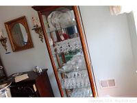 Cabinet display showing multiple shelves of clear etched glassware including plates, bowls, and glasses in June pattern.