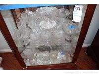 Full view of multiple shell and tassel pattern depression glass pieces on shelves including footed covered dishes, bowls, dishes, wine glasses, and plates.
