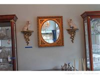Wide view showing the ornate gold framed mirror flanked by two gold-tone rococo style wall sconces each holding a Staffordshire dog figurine.