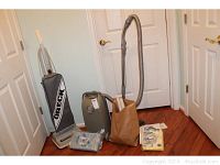 Photo of Oreck Classic XL upright vacuum cleaner, Kenmore Premier canister vacuum, and a brown paper bag containing attachments and bags.