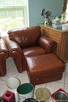 Photo of brown leather armchair with rolled arms and cushioned back next to kitchen cabinets and window.
