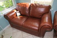 Brown leather loveseat angled to show left side and seating area near a window.