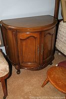 Pair of wooden half moon-shaped end tables with curved double doors and brass handles, showing minor scratches, placed beside beds.