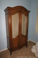 Full front view of carved wood armoire against wall