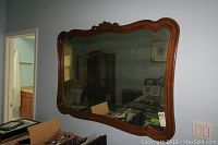 Full view of the large rectangular wall mirror with carved wood frame hanging on a light gray wall, showing overall design and size relative to surrounding furniture.