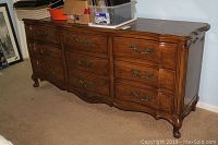 Full view of the large triple dresser showing nine drawers with ornate brass handles and carved legs.