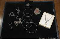 Top view of the entire assortment of sterling silver jewelry pieces arranged on black surface including rings, brooches, bangles, pin and a necklace in a box