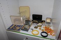 Assorted costume jewelry items on white surface including beaded necklaces, brooches, bangles and boxes, plus Russian belt buckle