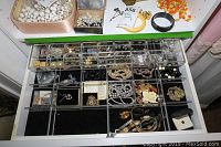 Clear plastic drawer organizer with multiple compartments holding assorted costume jewelry including necklaces, bracelets, earrings, and brooches.