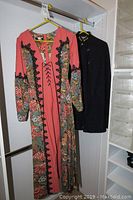 Side view of the vintage floral dress and black nurse cape hanging in a closet