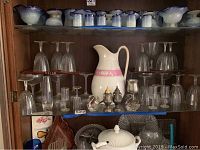 Full shelf display of wine glasses, champagne glasses, ceramic pitcher, silverplate swan condiment bowls, English metal goblet, and metal salt and pepper shakers.