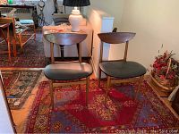 Two mid century modern style wooden chairs with semi-circular backrest and vinyl seats on a patterned rug, one chair with visible damage requiring repair.