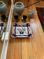 Photo showing the full set including the blue and white vase, small teapot, two metallic cups with saucers, and the decorative square tray on the floor near mirror reflection.