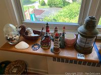 Wide shot of all items on windowsill including the lantern, six lighthouse figurines, bowl with seashells, carved duck figure, pottery bowl, and large seashell.