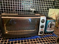 Euro-Pro toaster oven and Oster two-slice toaster on kitchen counter with black tiled backsplash. Oven has three control knobs and metal rack inside.
