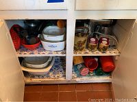 Two shelves containing various kitchen items including Corningware dishes, measuring cups, colanders, ceramic teapot, and kitchen utensils.
