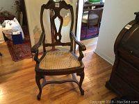Front view of vintage carved wood chair with caned seat, showing carved backrest, curved armrests, and caned seating area.