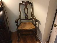 Front view of the vintage carved wood chair showing carved details, armrests, and caned seat