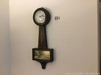 Full view of the Gilbert banjo wall clock hanging on the wall showing painted floral design and country scene on bottom box.