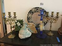 View of both brass candelabras, Venetian blue glass candlestick, ceramic vase, frog planter, and large ceramic platter on black surface.