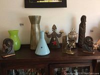 Overall view on sideboard: left ram bookend, green glass vase, hammered metal vase, light blue ceramic vase, metal candle holder, porcelain urn, wooden figure, right ram bookend